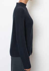 Maglione lavorato a maglia di un blu navy scuro con collo alto, maniche lunghe e finitura testurizzata. Presenta una linea dritta e un dettaglio con zip laterale.