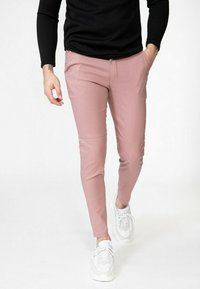Pantalons roses slim en matière tissée, dotés de poches latérales, portés avec un haut noir à manches longues et des baskets blanches.