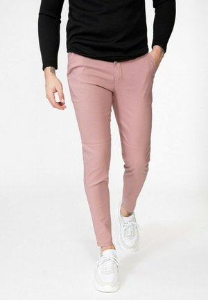 Pantalons roses slim en matière tissée, dotés de poches latérales, portés avec un haut noir à manches longues et des baskets blanches.