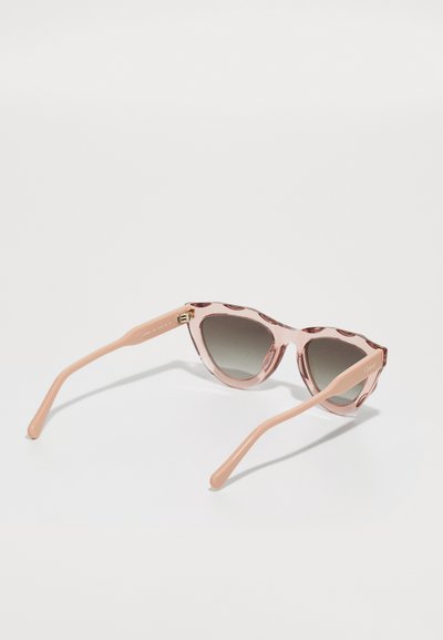 Lunettes de soleil cat-eye avec une monture translucide rose et des verres gris dégradés. Présente un motif floral subtil et des accents en métal doré.