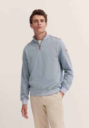 Helles blaues Zip-Pullover aus strukturiertem Stoff. Mit hohem Kragen, gerippten Bündchen und einem kontrastierenden grauen Saum.
