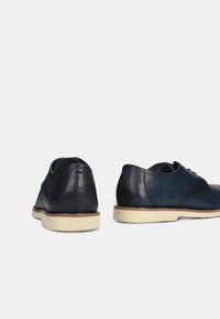 Pantofi din piele de culoare bleu închis și negru, cu șireturi, vârf rotunjit și tălpi din cauciuc de culoare deschisă. Textură netedă cu detalii minime.