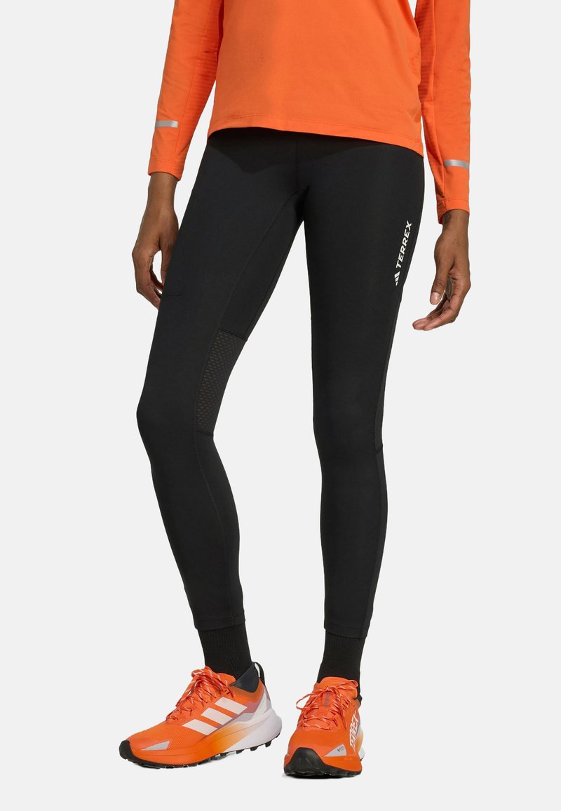 Svarta sportiga leggings med en figurnär design, utrustade med mesh-paneler och reflekterande detaljer. I kombination med oranga skor och topp.