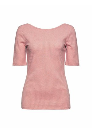 Vrouw draagt een zwarte doorgestikte jas, een roze geribd topje, hoge grijze jeans met zwarte riem en witte sneakers, staand tegen een effen achtergrond.