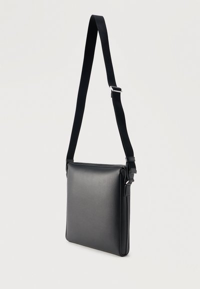 Μαύρη δερμάτινη τσάντα χιαστί με ρυθμιζόμενο μαύρο υφασμάτινο λουράκι και ασημένια πόρπη, ορθογώνιο σχήμα, μινιμαλιστικός σχεδιασμός.