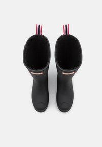 Bottes de pluie en caoutchouc noir avec une texture lisse, dotées d'une doublure en polaire noire et d'une languette de tirage rayée rouge et blanche en haut.