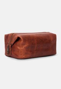 Brown leather travel bag with a rectangular shape, zip closure, and smooth, slightly textured surface. Notable hardware accent on zipper.