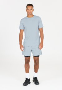 Vaaleanharmaa urheilupaita ja shortsit, jotka on valmistettu kosteutta siirtävästä kankaasta. Ominaisuuksiin kuuluu pyöreä kaula-aukko ja hillitty painatus rinnassa.