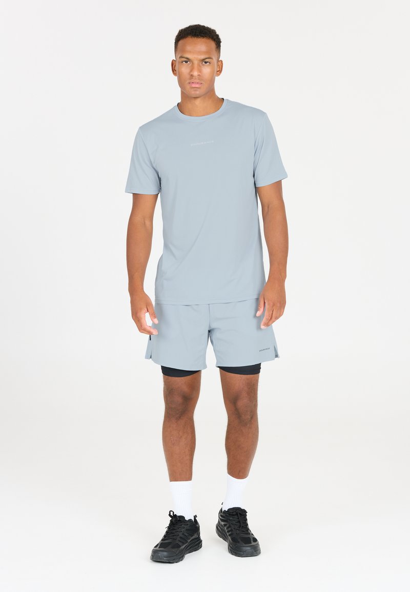 Vaaleanharmaa urheilupaita ja shortsit, jotka on valmistettu kosteutta siirtävästä kankaasta. Ominaisuuksiin kuuluu pyöreä kaula-aukko ja hillitty painatus rinnassa.