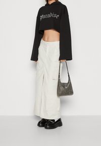 Sweat à capuche noir court avec le texte « Paradise », jupe cargo blanche fendue, chaussures plates-formes noires, et sac à main métallique.