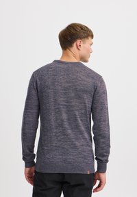 Maglione lavorato a maglia di un blu scuro con texture mista, scollo rotondo e polsini a coste. Presenta un piccolo accento in pelle all'orlo.