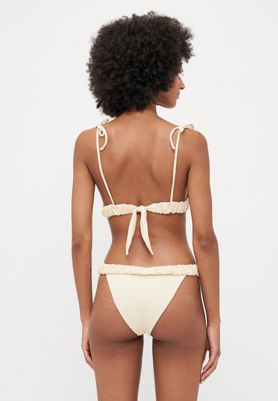 Cremfarbener Bikini mit strukturiertem Stoff, verstellbaren Trägern am Oberteil und Rüschendetails am Bund des Unterteils.