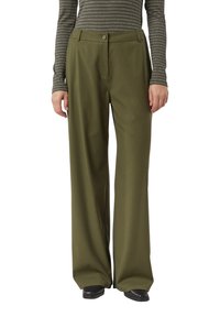 Spodnie o szerokich nogawkach z oliwkowej tkaniny o miękkiej fakturze. Posiadają zapięcie na guziki z przodu i szlufki na pasek. Noszone z paskowaną bluzką z długim rękawem.
