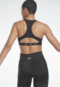 Sujetador deportivo negro con diseño de espalda nadadora, que presenta un corte y una banda elástica con marca. Combinado con leggings negros de cintura alta con detalles laterales.
