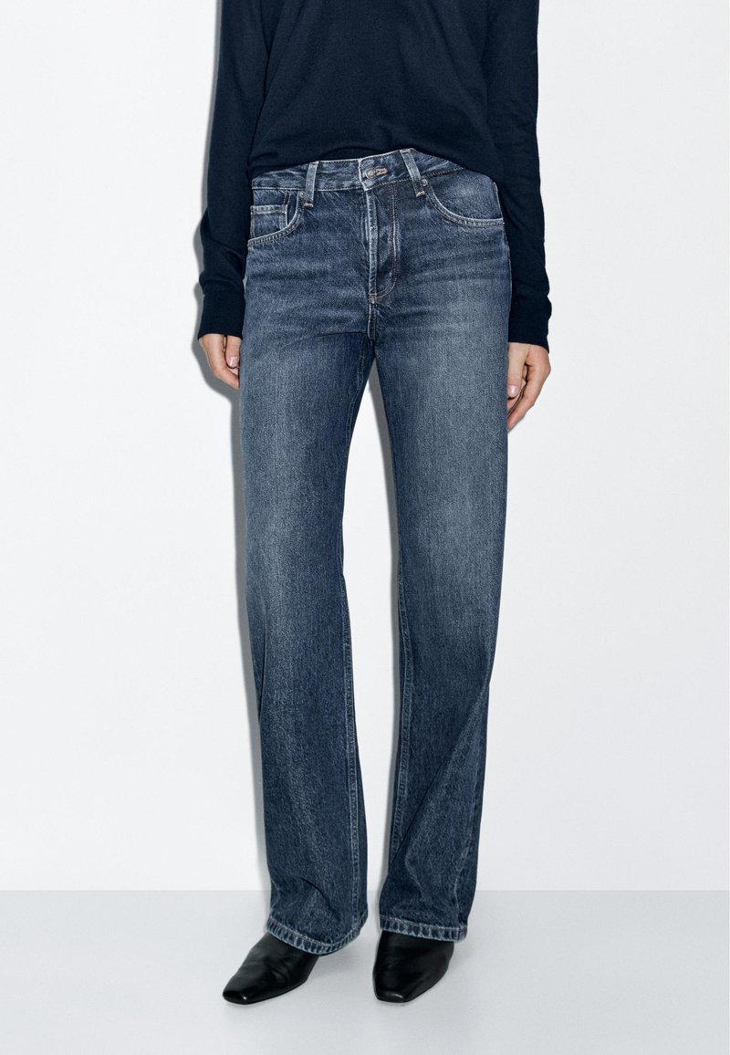 Mørk vask denim jeans med lige ben-design, der har forlommer og subtile stikningsdetaljer. Sættes sammen med sorte spidse sko.