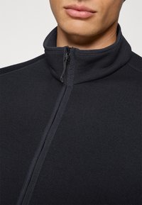 Giacca in pile blu navy con colletto alto, zip intera e texture a coste. La vista ravvicinata mette in evidenza i dettagli del tessuto e le cuciture.