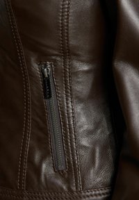 Pruuni nahkjope, millel on tõmblukuga tasku. Materjal on sile, peenete õmblustega õmbluste juures ja läikiv tõmblukk.