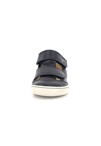 Zapato de cuero azul marino con dos correas de velcro, suela de goma blanca, acentos cosidos y secciones recortadas para transpirabilidad.