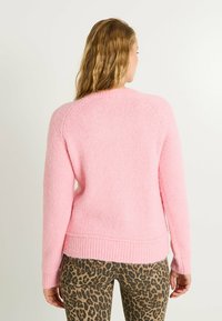 Pull en tricot rose avec une finition texturée, ourlet en côte et manches raglan, associé à un pantalon à motifs léopard.