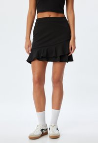 Zwarte rok met een gelaagd ruches ontwerp, aansluitende taille, gemaakt van een katoenmix stof, gecombineerd met witte sokken en sneakers.