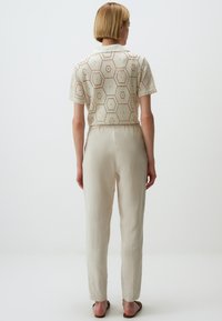Haut en tricot hexagonal crème à manches courtes, coupé, associé à un pantalon beige clair et fuselé. Caractérisé par une coupe décontractée et une texture douce.