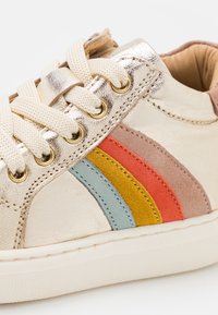 Kremowe skórzane sneakersy z metalicznymi akcentami, z wielokolorowymi zamszowymi paskami: czerwonym, żółtym, niebieskim i różowym. Beżowe sznurówki i gumowa podeszwa.