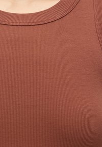 Gros plan d'un haut sans manches côtelé couleur rouille montrant l'encolure et la texture du tissu.