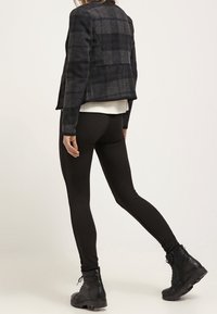 Leggings neri abbinati a una giacca a quadri scuri. La giacca presenta un design aderente e una trama sfumata. Indossata con stivali neri alla caviglia.