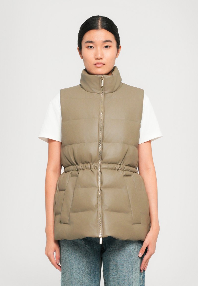 Gevoerde vest in olijfgroen met hoge kraag, ritssluiting aan de voorkant, elastische tailleband en twee voorkruiszakken. Draag het over een wit shirt en denim jeans.