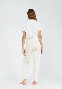 Camiseta blanca combinada con pantalones de tiro alto de corte recto en beige claro. Bolsillos traseros visibles y un diseño minimalista.