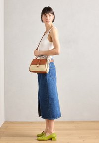 Tan and straw handbag with a brown trim and strap. Blue denim skirt with side slit. Green heeled shoes. White tank top. Simple design.