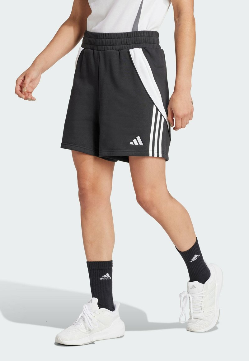 Pantaloni corti sportivi neri con pannelli laterali bianchi e tre strisce bianche, dotati di una cintura elastica. Abbinati a calzini neri e sneakers bianche.