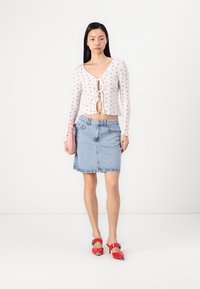 Hvit langermet topp med små blomsterdetaljer, knyttet foran; blå denim A-linjett skjørt; rosa clutch; røde høye hæler med spiss tå.