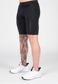 Zwarte sportshorts met een aansluitend ontwerp, gemaakt van rekbaar materiaal. Bevat reflecterende accenten aan de zijkanten, gecombineerd met witte sneakers.