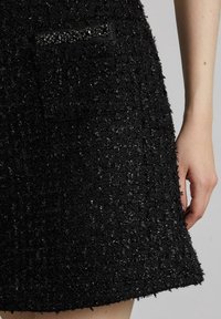 Falda negra texturizada con una tela peluda y detalles metálicos. Incluye un pequeño bolsillo con adornos decorativos.