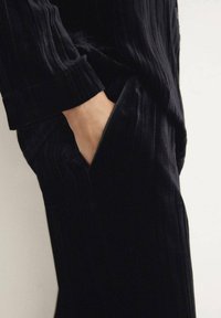 Prenda de tela texturizada negra con rayas verticales, que incluye un bolsillo lateral y un ajuste relajado en la cintura y los puños.