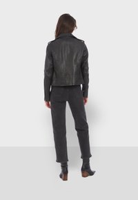 Black leather biker jacket with zip cuffs, structured shoulders, and back seams. Paired with dark jeans and heeled boots.
