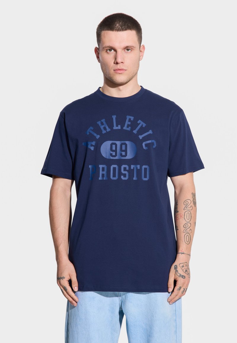 Granatowa bawełniana koszulka z okrągłym dekoltem, z nadrukiem tekstu "ATHLETIC 99 PROSTO" w ciemnoniebieskim kolorze, krótkie rękawy, luźny krój.