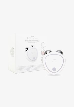 Hvid trekantet ansigtstoningsenhed med sølvfarvede accenter og en central tænd/ sluk-knap, vist sammen med sin mærkede emballage.