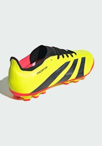 Botín de fútbol amarillo brillante con acentos negros, que presenta un diseño elegante, superficie texturizada y detalles rojos. Suela de goma ligera con tacos.