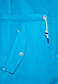 Giacca impermeabile blu brillante con tasca a scatto, coulisse bianca e dettagli in acciaio inox. Superficie liscia, design minimalista.