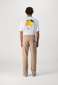 White t-shirt with fruit graphic in yellow and orange; beige cargo pants with pockets; visible stripes on shoes, minimalistic design.