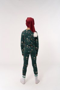 Grüne Baumwollpyjamas mit festlichen Motiven, kombiniert mit einem roten gestrickten Weihnachtsmannhut mit einem weißen Bommel. Weiße Socken runden das Outfit ab.