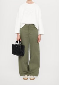 White sweatshirt with embroidered design, paired with loose olive-green pants. Features a black woven handbag and beige shoes with tan soles.