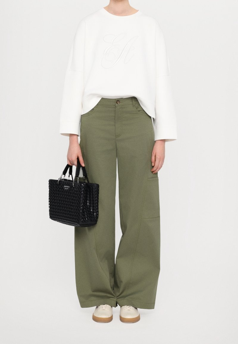 White sweatshirt with embroidered design, paired with loose olive-green pants. Features a black woven handbag and beige shoes with tan soles.