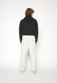 Svart hoodie med bakficka, tillsammans med krämfärgade joggers med sidfickor och elastiska muddar. Sneakers i ljusgrå.