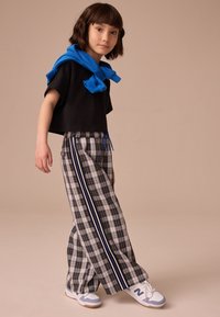 T-shirt noir court, pantalon large à carreaux gris avec des rayures bleues, et baskets blanches. Tissu texturé, coupe décontractée, avec taille à cordon.