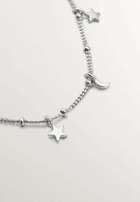 Collar de cadena de plata con eslabones retorcidos, adornado con charms de estrella y luna creciente. Textura suave y acabado pulido.