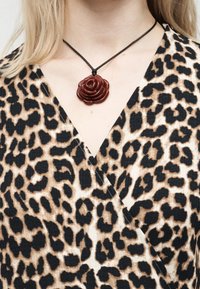 Κοντινό πλάνο στήθους που φοράει τοπ με λεοπάρ σχέδιο και μπρονζωμένο μενταγιόν σε σχήμα σκοτεινού κόκκινου τριαντάφυλλου σε κολιέ με μαύρο κορδόνι.