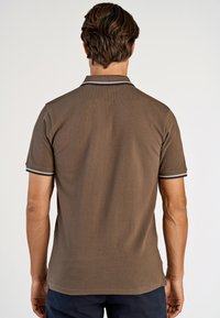 Brun pikétröja med en texturerad tyg, korta ärmar, krage och marinblå och vita ränder längs kragen och ärmsluten.